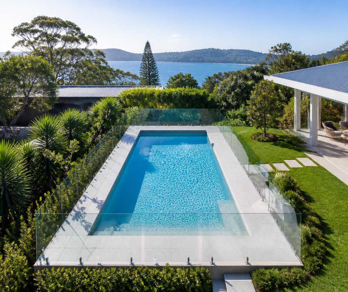 Aerial view of a coastal property with frameless glass pool fencing overlooking the water